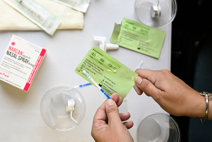 two hands hold fentanyl test strip over a table of other testing items