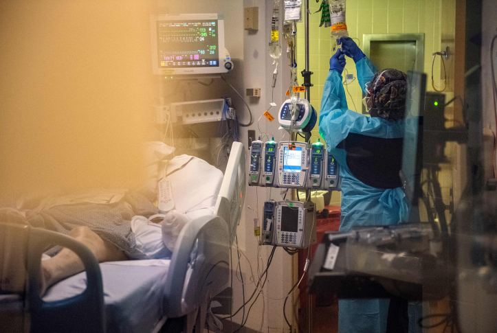 hospital worker changes IV bag next to patient in hospital bed