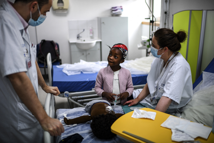 Girl sits on hospital bed with two hospital staffers