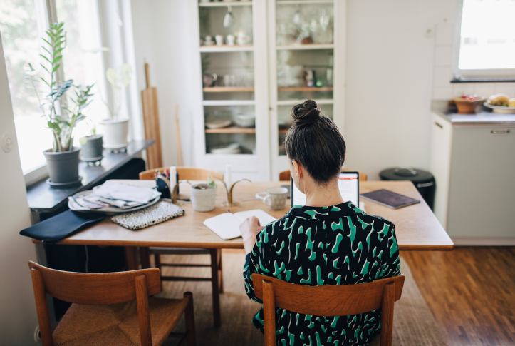 Woman sits at table with laptop and book out in front of her in her home