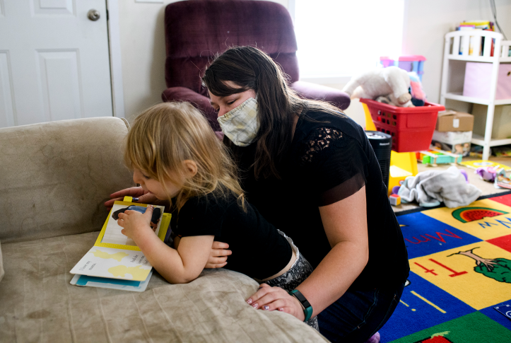 Photo, woman wearing mask reading book with autistic child on couch