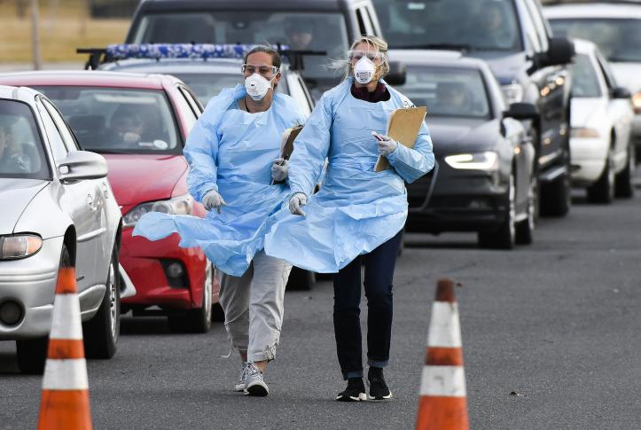 Health workers walking through a line of cars waiting for coronavirus tests