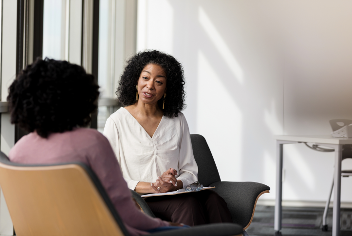 Photo, woman talking to other woman, with clipboard in lap