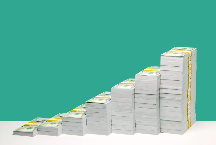 Stacks of U.S. hundred dollar bill bundles in ascending order on white shelf, green background.