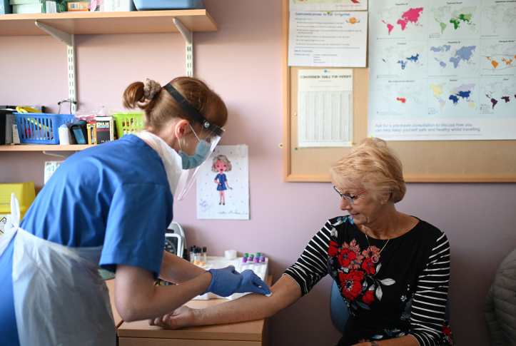 Photo, nurse in PPE takes blood sample from patients arm in doctors office.