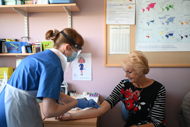 Photo, nurse in personal protective equipment takes blood sample from patient's arm in doctors office