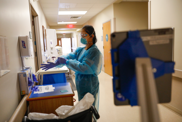 Photo, nurse puts on gloves while wearing full PPE