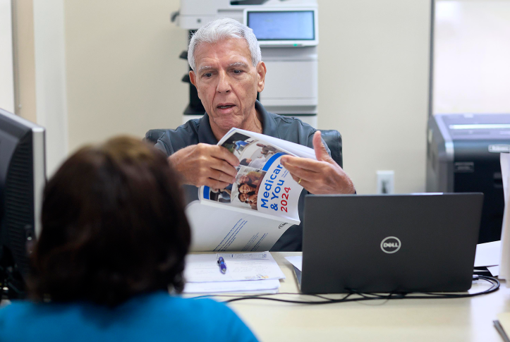 Man opens brochure for woman in front of computer