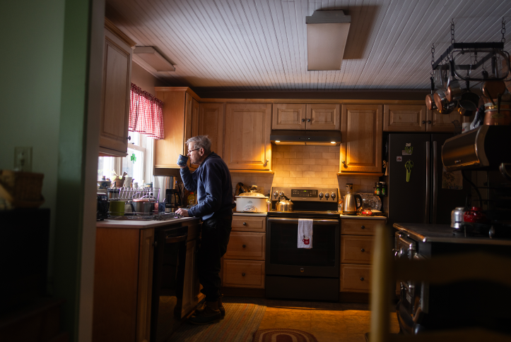 Elderly man drinking from coffee cup staring out kitchen window