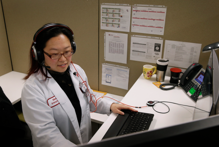 Woman in lab coat and headset talks while using computer