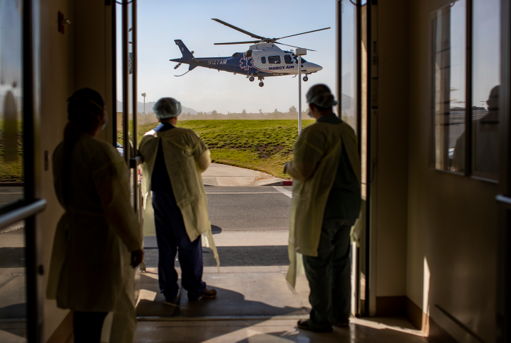 Three medical staff stand in front of open door staring at a helicopter