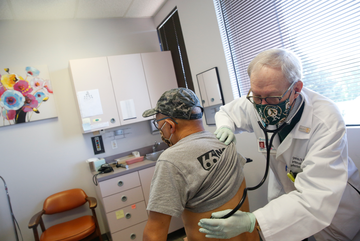 Doctor examines patient in doctors office while both wear masks