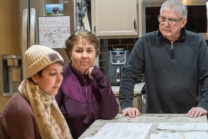 Three people look at bills on counter in kitchen