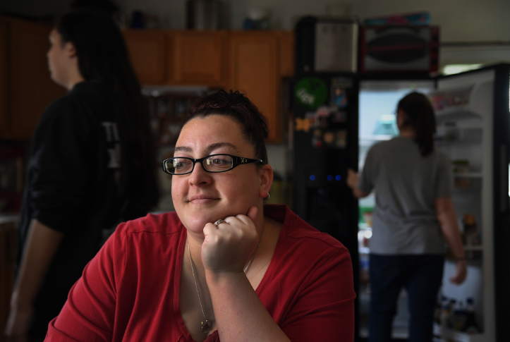 Woman sits in a dark kitchen surrounded by children looking contemplative