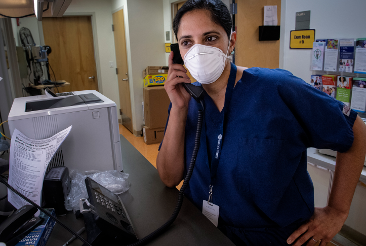 Female physician in scrubs and mask on phone in hospital