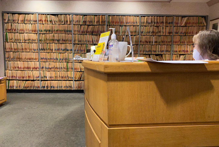 Receptionist sitting at desk next to wall of medical records