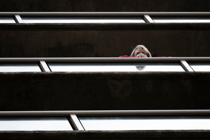 Mask-wearing senior stairs out of balcony in senior living community.