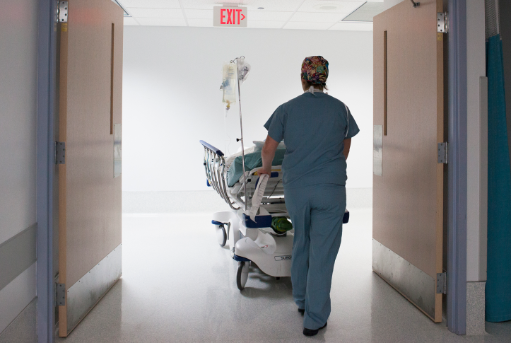 Photo, back of hospital staff person pushing medical bed