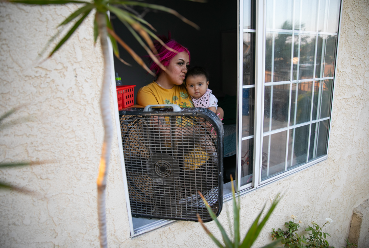 Woman and child stand in front of fan in open window