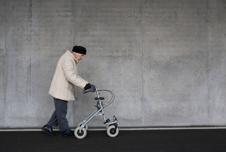 Elderly woman walking in coat with walker against a plain background