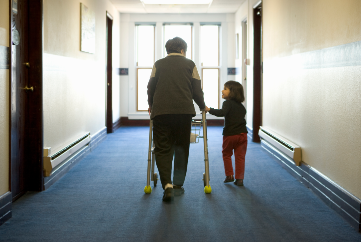 Elderly woman with walker is helped down hallway by young girl