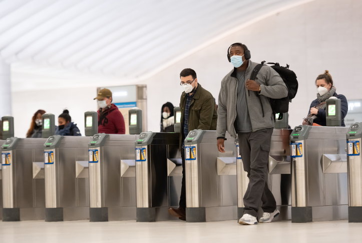 Commuters walk thru terminal in station with masks.