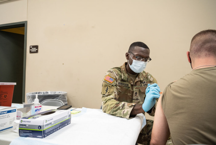 Military doctor gives vaccine to other military member at white table