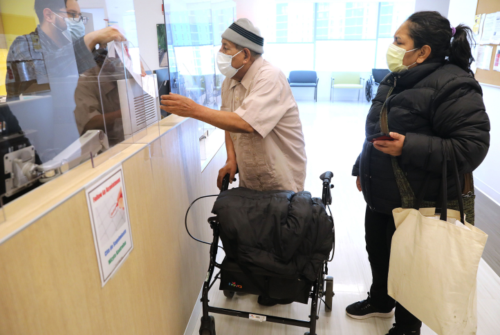 Man in mask with walker gets paperwork from clinic desk.