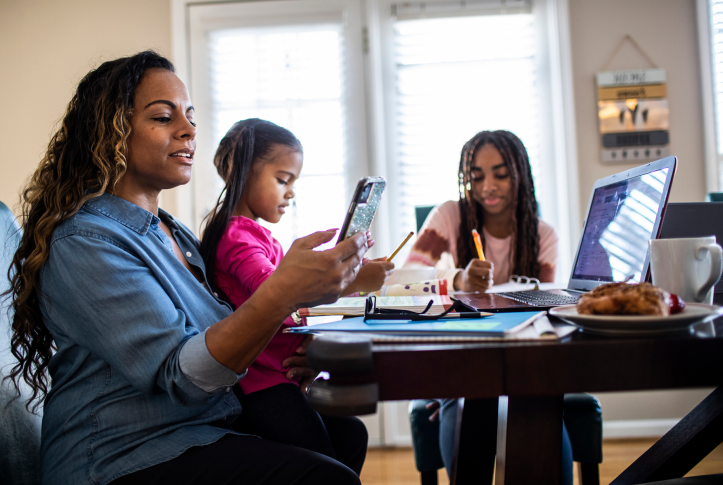 Mom and two daughters sit at dining room table working on computers and school work