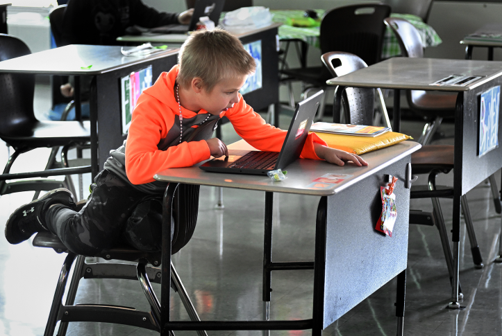 Photo, child leans over school desk with laptop