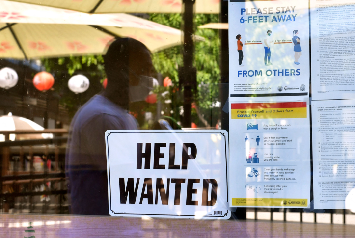 A “Help Wanted” sign is posted beside coronavirus safety guidelines in front of a restaurant