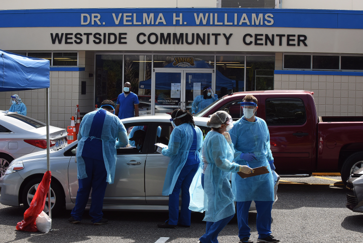 Doctors in scrubs and gowns wait outside cars outside of Dr. Velma H. Williams Westside Community Center