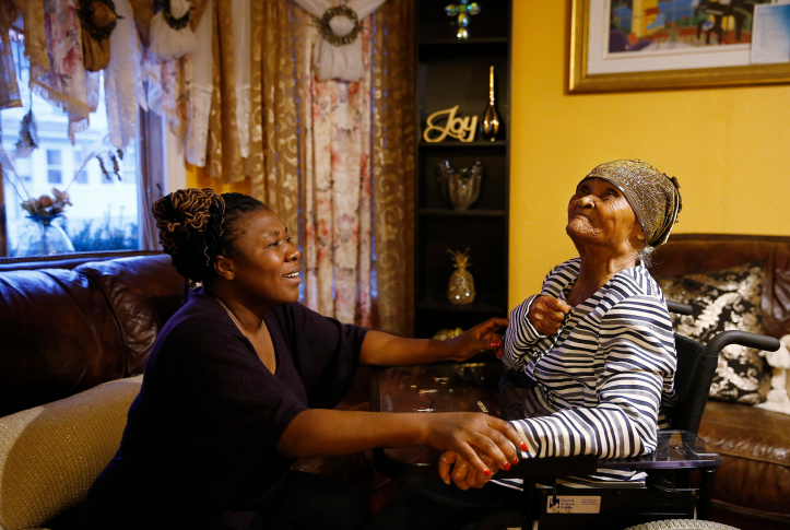 Photo, woman holds hands of older woman in home