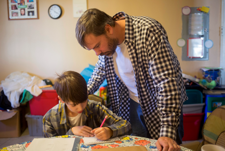 Man helps young boy with homework at a table.