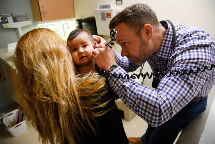 Doctor looks in baby's ear in doctors office while mother holds baby