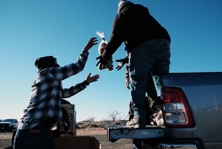 Man tosses bag of potatoes to person on a truck