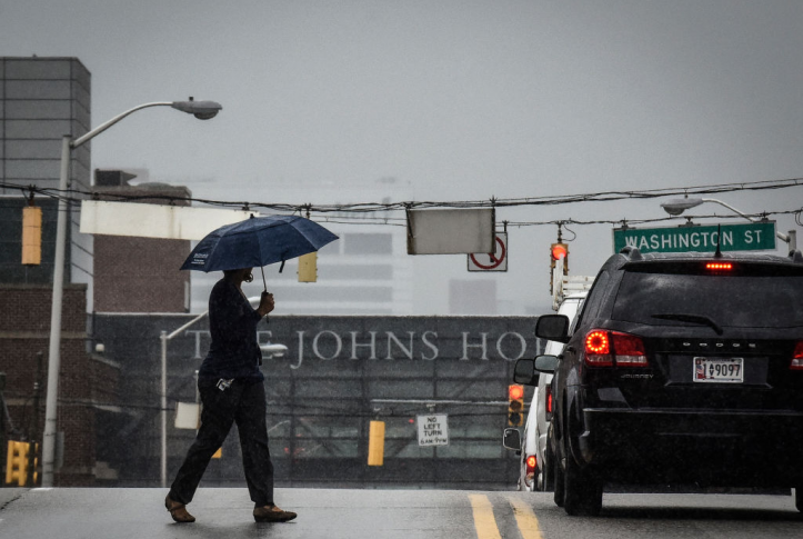 Pedestrian crosses with umbrella in front of Johns Hopkins hospital