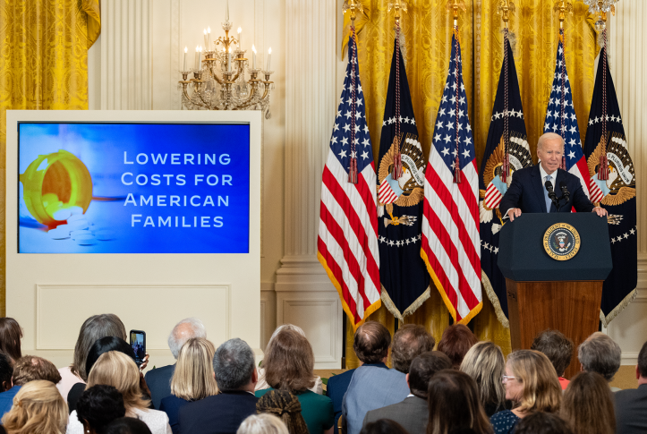 Photo, President Biden at podium in front of flags and powerpoint presentation on lowering costs for American families