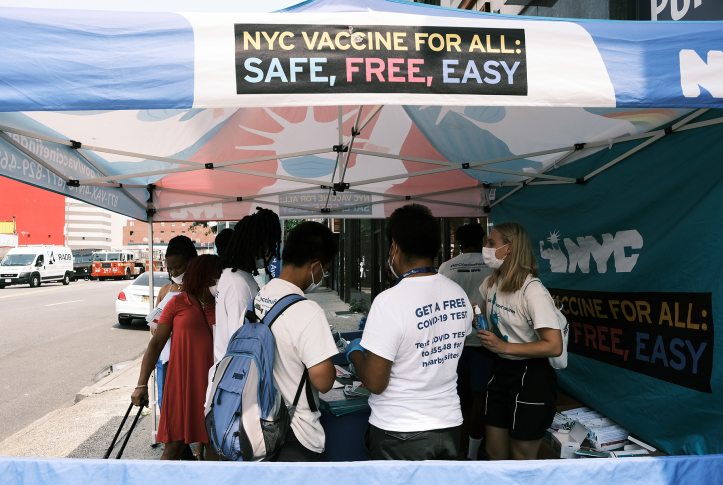 People stand in front of NYC free vaccine sign under a tent