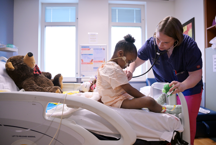 Doctor uses stethoscope on young girl in hospital bed