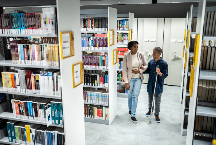 Photo, man with cane walks holding woman's arm in library