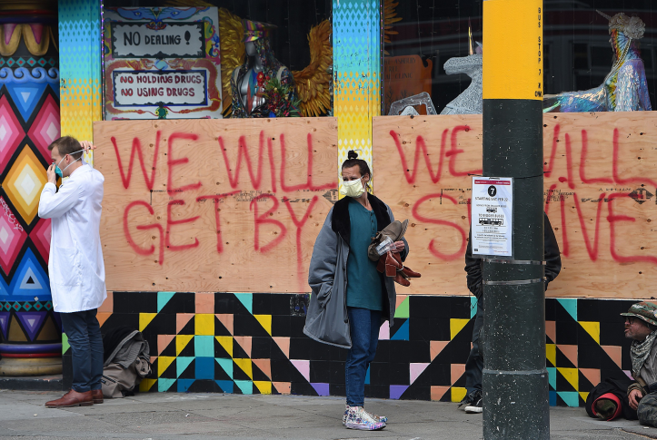 Stuart Malcolm (L), a doctor with the Haight Ashbury Free Clinic, puts on a mask before speaking with homeless people in front of a boarded-up shop.