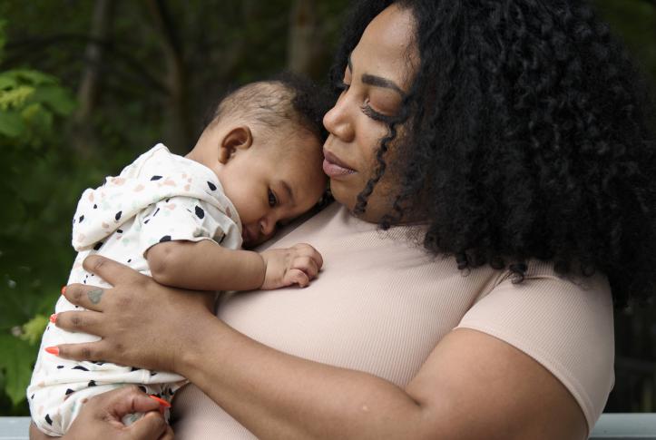 Mother cradling five-month-old son in arms outside home