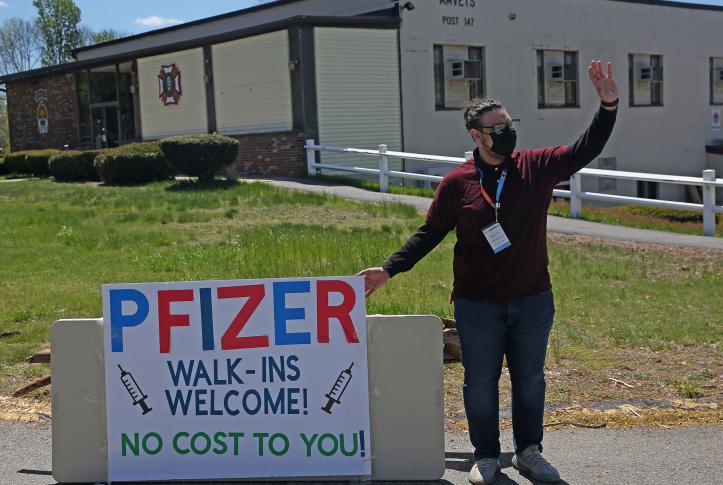 A site specialist employee with Curative holds a Pfizer sign and waves to passing cars in Haverhill, Mass., on May 6, 2021.