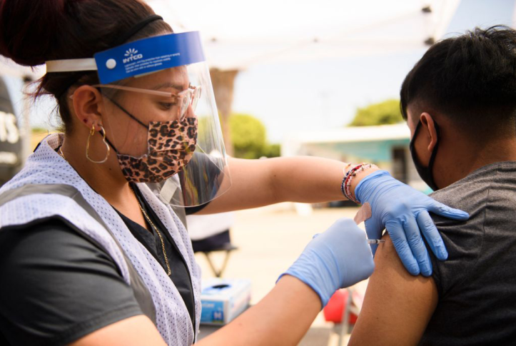 Nurse with mask and face shield gives young teen a COVID vaccine
