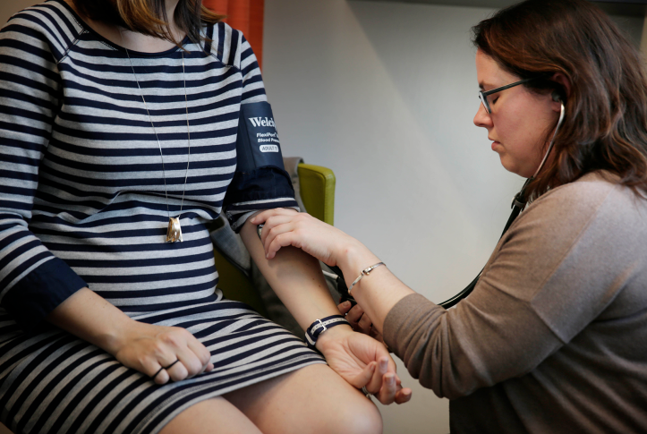 doctor checks female pregnant patients bloodpressure with cuff