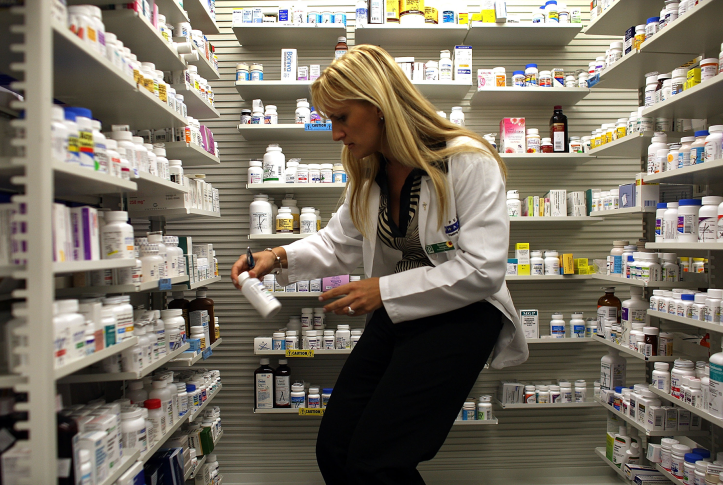 A pharmacy manager retrieves a bottle of antibiotics from the shelf