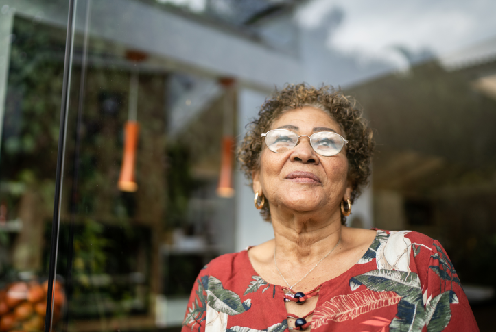 elderly woman in glasses looks up at sky in front of house