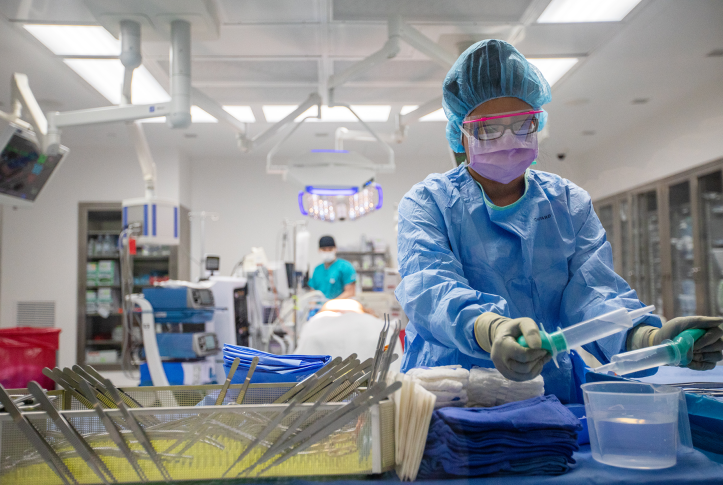 Photo, surgeon in PPE cleans instruments in operating room.