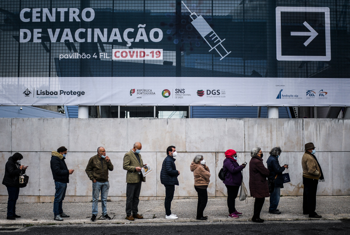 Masked people stand in line for vaccine in front of vaccination sign in Portuguese